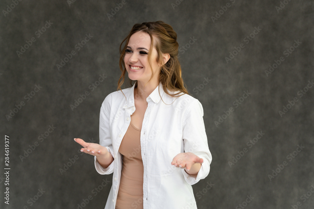 Photo waist-length portrait of a pretty brunette woman girl with long beautiful curly hair on a gray background in a white shirt. Talking in different poses. Standing facing the camera. Photo waist-length portrait of a pretty brunette woman girl with long beautiful curly hair on a gray background in a white shirt. Talking in different poses. Standing facing the camera.