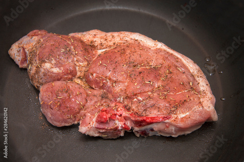 Fresh raw pork steak with spices roasting on the black frying pan in the kitchen