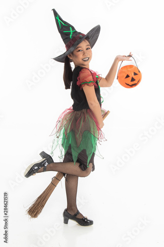 Portrait of little Asian girl in Halloween witch costume and black hat with pumpkin and broom on white isolated background