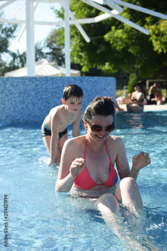 Mom and son playing and splashing in a swimming pool. Family on a pool in hot summer day © Ivan