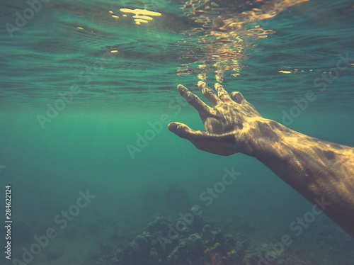 Underwater hand reaching for sun. Man drowning in the sea. Rescue from swimming pool accident. Sinking under the water. Shipwreck survivor. Need help. Believe in your self. Quote background template.