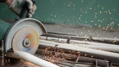 A man cuts metal pipes, slow motion video. sparks fly in all directions. Low light image of Worker ware yellow helmet kneel use electric steel cutter machine. He has a Hard work in Factory or garage. 