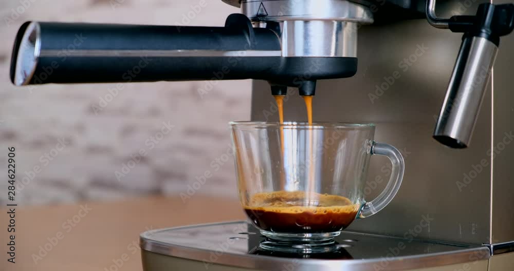 Pouring coffee stream from professional machine in cup. Making double espresso, using filter holder. Flowing fresh ground coffee. Drinking roasted black coffee in the morning. Thick aromatic drink wit Pouring coffee stream from professional machine in cup. Making double espresso, using filter holder. Flowing fresh ground coffee. Drinking roasted black coffee in the morning. Thick aromatic drink wit