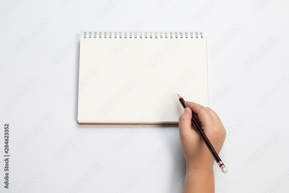 Top view little Asian boy hand or schoolboy kid writing on black paper mock up with many colorful pencils on white table background Top view little Asian boy hand or schoolboy kid writing on black paper mock up with many colorful pencils on white table background