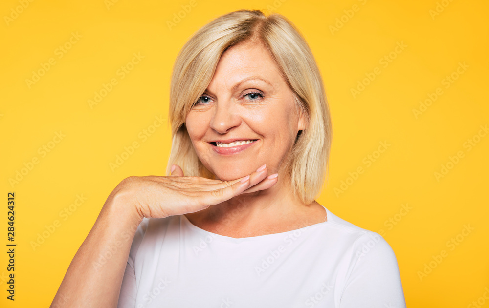 Happy smiling beautiful cute lovely blonde senior woman with beauty clean skin in casual wear isolated on yellow background. Healthcare and cosmetology concepts. Pensioner and mature people Happy smiling beautiful cute lovely blonde senior woman with beauty clean skin in casual wear isolated on yellow background. Healthcare and cosmetology concepts. Pensioner and mature people