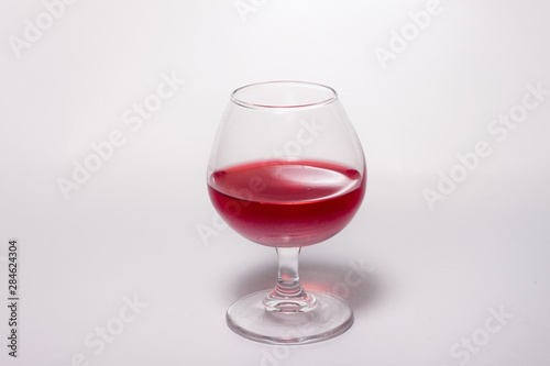 Glass goblet with red drink on a white background. With a shadow from a glass of Minimalism.