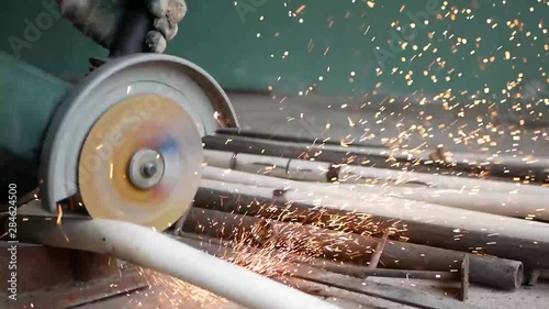 A man cuts metal pipes, slow motion video. sparks fly in all directions. Low light image of Worker ware yellow helmet kneel use electric steel cutter machine. He has a Hard work in Factory or garage. 