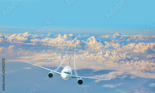 Aircraft flies high over the city and and sea coast -  White passenger airplane in the clouds at sunset - Travel by air transport