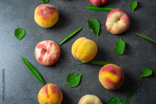 Nice yummy fresh peaches with green tree leaves on dark texture surface. Top view. Summer fruits.