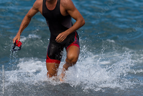 Triathlete swimmer running out of ocean finishing swim race.Fit man ending swimming sprinting determined out of water in professional triathlon suit for ironman