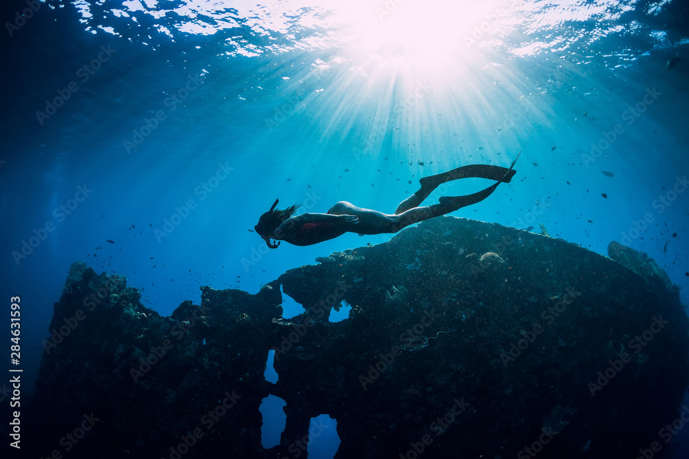 Woman freediver glides with fins at wreck ship. Freediving in blue ocean near wreck - obrazy, fototapety, plakaty 