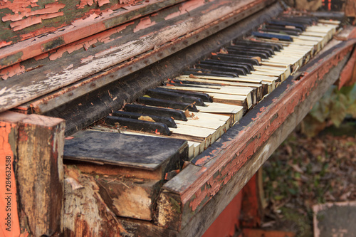 An old broken piano covered with fallen leaves, autumn outdoors.