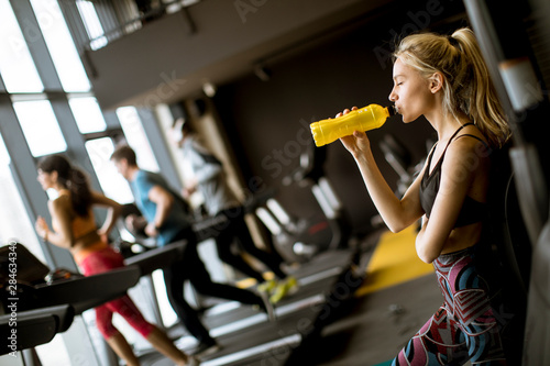 Young woman drinking water in gym after workout