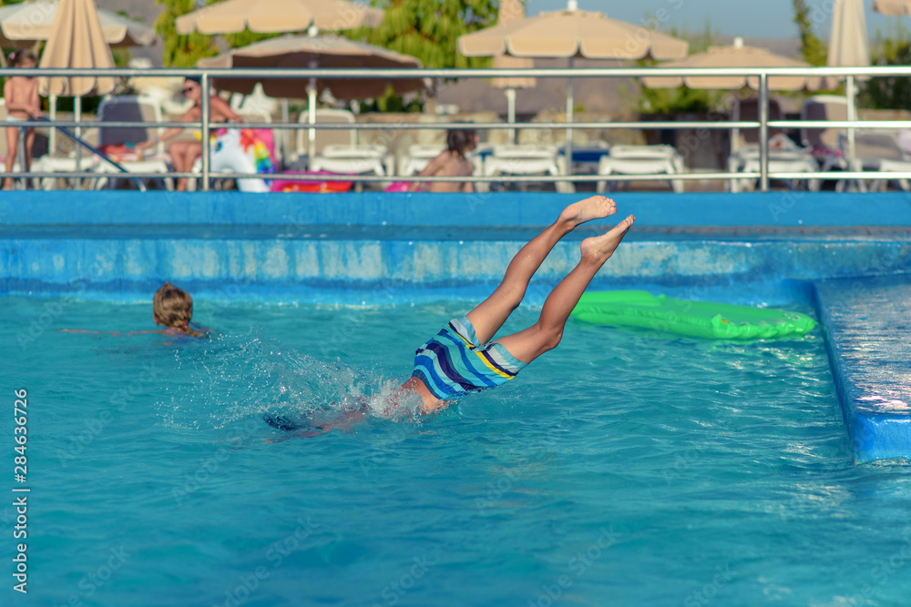 Portrait of  Caucasian boy spending time in pool at resort during his summer vacations.  He is jumping in to the water.
