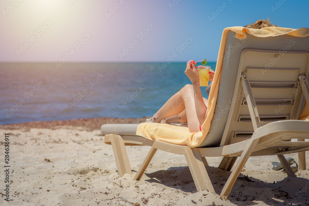 Woman is laying on a sunbed at the luxurious hotel near sea, she is enjoying her summer vacations and holding a glass of cocktail in her hand.