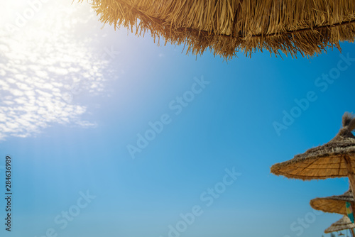 Summertime. Straw sun umbrellas at the beach against wonderful blue sky. Background, copy space.