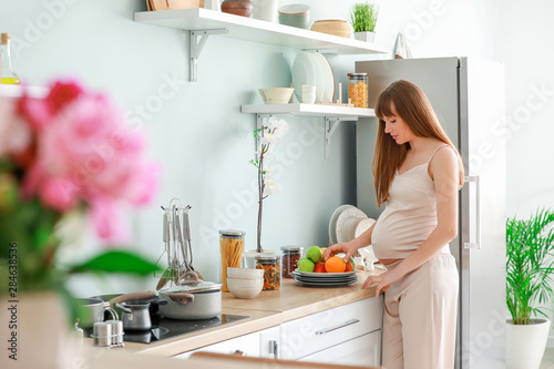 Beautiful pregnant woman with fruits in kitchen