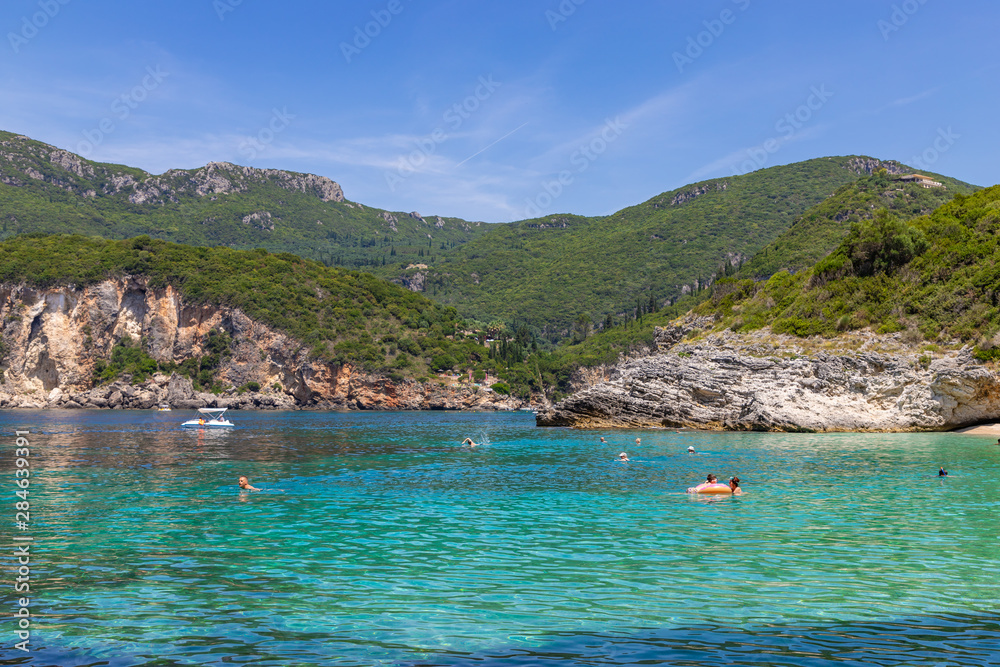CORFU / GREECE - JUNE 22, 2019: People visit famous Rovinia beach with clear water in Corfu Island.