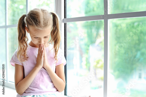 Praying little girl near wi...