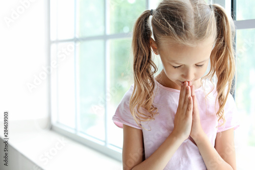 Praying little girl near wi...
