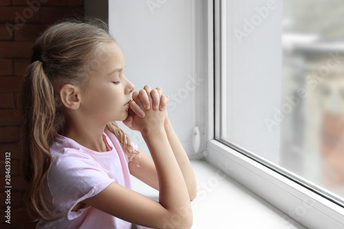 Praying little girl near wi...