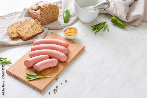 Board with tasty sausages, bread and sauce on light table
