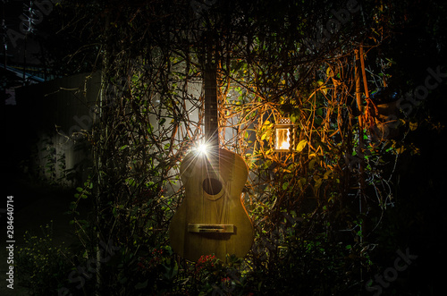 An wooden acoustic guitar is against a grunge textured wall. The room is dark with a spotlight for your copyspace. photo