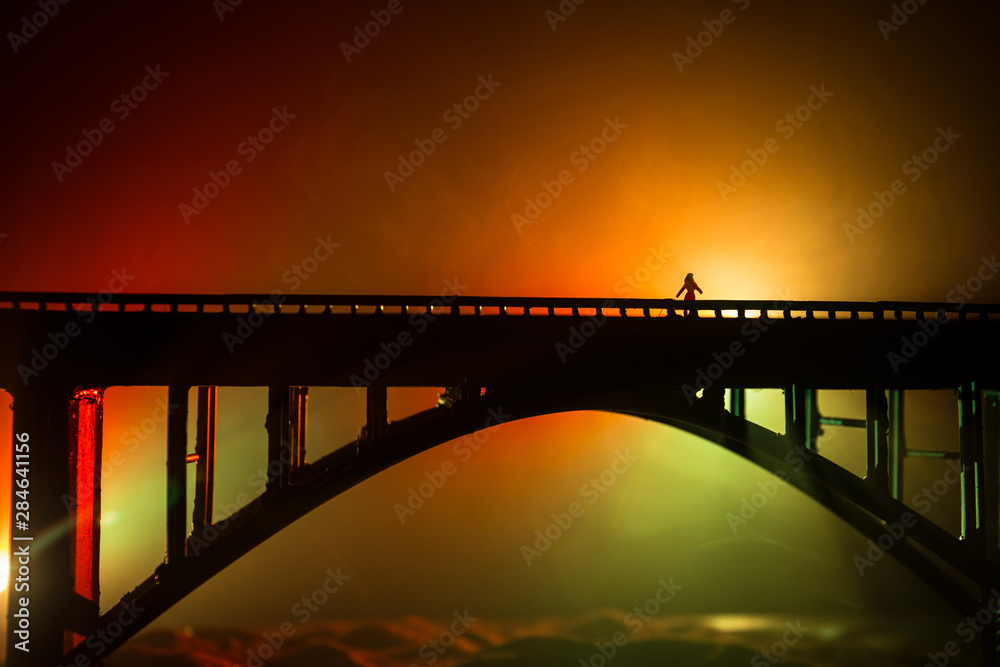 Obraz premium Artwork decoration. Silhouette of powerful metallic bridge at night with foggy backlight. Silhouette of person standing on bridge.