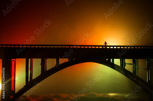 Fototapeta Naklejka Na Ścianę i Meble -  Artwork decoration. Silhouette of powerful metallic bridge at night with foggy backlight. Silhouette of person standing on bridge.