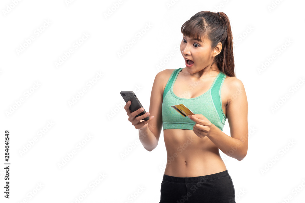 Fitness woman using mobile phone and holding credit card isolate in white background. Asian girl, surprise look. Fitness woman using mobile phone and holding credit card isolate in white background. Asian girl, surprise look.