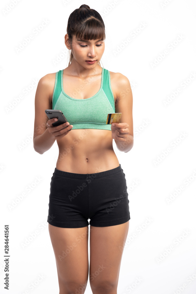 Fitness woman using mobile phone and holding credit card isolate in white background. Asian girl, trying to focus.