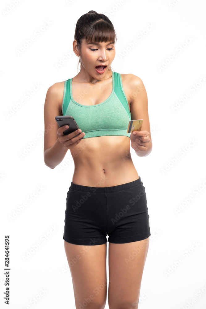 Fitness woman using mobile phone and holding credit card isolate in white background. Asian girl, very shock look. Fitness woman using mobile phone and holding credit card isolate in white background. Asian girl, very shock look.