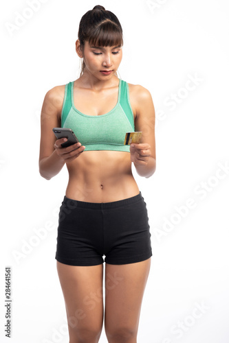 Fitness woman using mobile phone and holding credit card isolate in white background. Asian girl, trying to focus. © Baan Taksin Studio