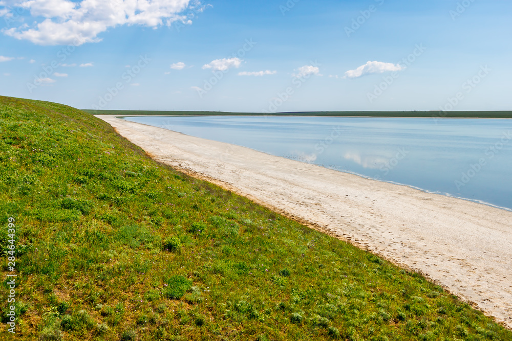 Fototapeta premium The view of the waterside of the drying up salt lake with green grassy hills on the bank. Gruzskoe lake, Rostov-on-Don region, Russia