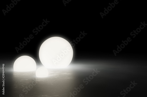 Three warm glowing sphere light objects on shiny modern industrial concrete floor in dark room with copy space - 3D illustratrion photo