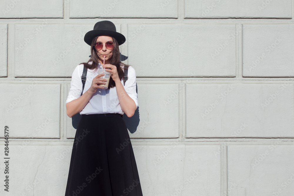 Young woman in hat and round sunglasses walking in city. Girl tourist enjoys the walk. Young woman in hat and round sunglasses walking in city. Girl tourist enjoys the walk.