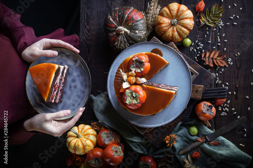 Autumn cake with persimmon and caramel with a pumpkin and a girl in a burgundy dress on a black background, Atmospheric dark food photos, Pastry Homemade in Womans hands, Selective focus