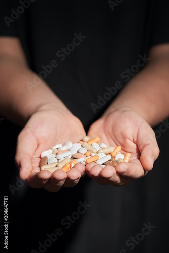 Kid holds heap of colorful pills and drugs in his hand palm on dark moody background. Concept of drug addiction and suicide.