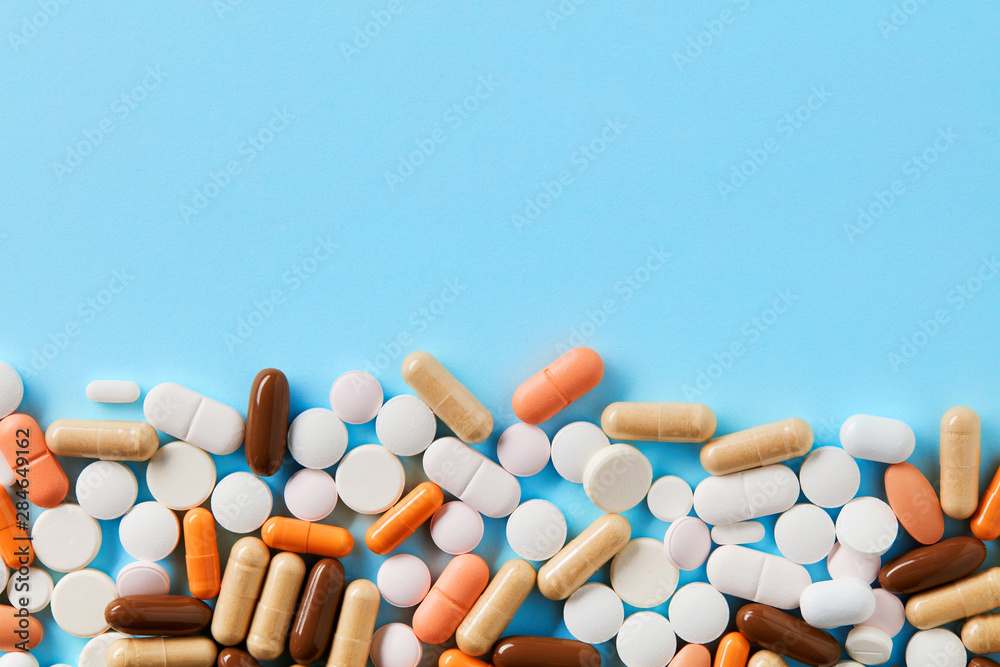Heap of of colorful pills tablets and capsules on blue background with copy space for text. Top down view. Heap of of colorful pills tablets and capsules on blue background with copy space for text. Top down view.