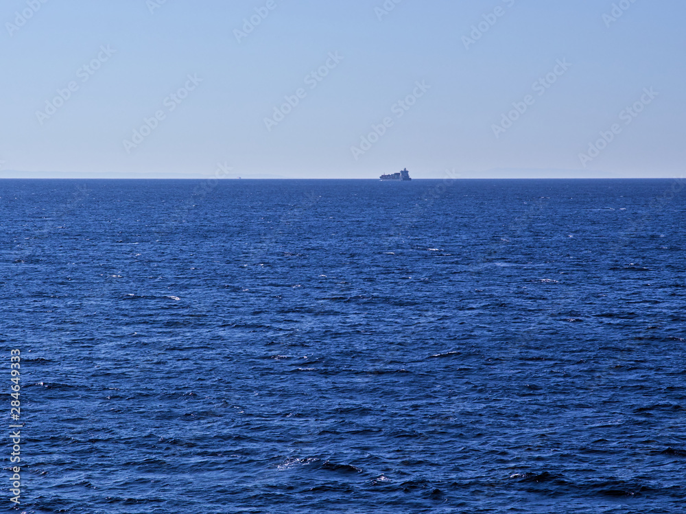 Distant cargo ship sailing at textured sea.