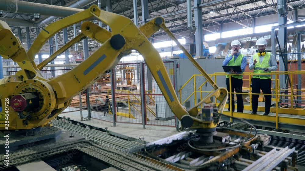 Modern industrial robotic arm and two experts talking near it.