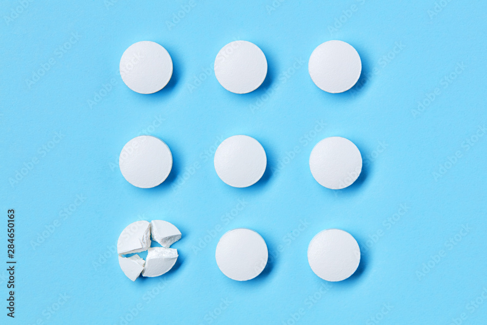Round white medical pills arranged in square order and one of them is crushed into four parts. Pill splitting. Round white medical pills arranged in square order and one of them is crushed into four parts. Pill splitting.