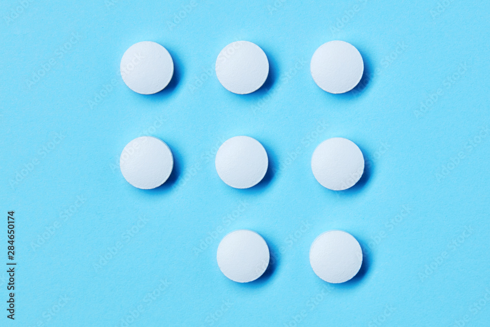 Round white medical pills on blue background with copy space. Regular daily drug use.