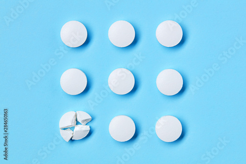 Round white medical pills arranged in square order and one of them is crushed into four parts. Pill splitting.