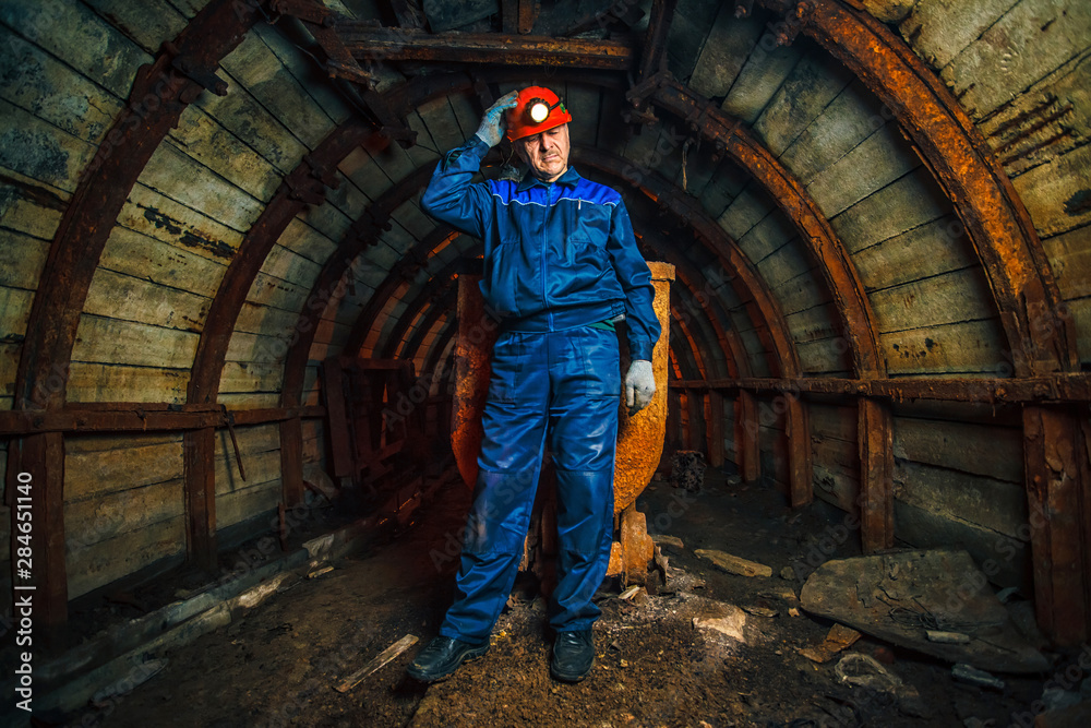A miner in a coal mine stands near a trolley. Copy space. A miner in a coal mine stands near a trolley. Copy space.
