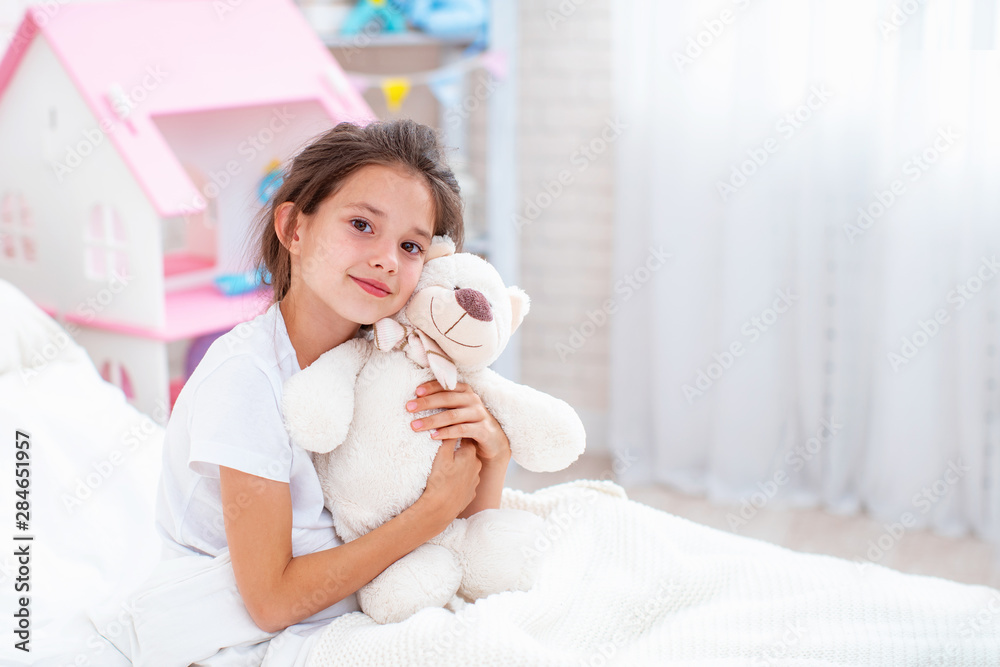 happy cheerful young girl sitting on the bed holding a Teddy bear in front of a Saba happy cheerful young girl sitting on the bed holding a Teddy bear in front of a Saba