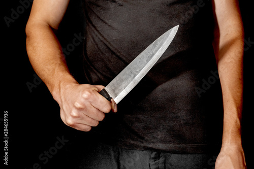 Man's hand holds a knife on black background. topics of violence and murder. thief, killer, rapist, maniac