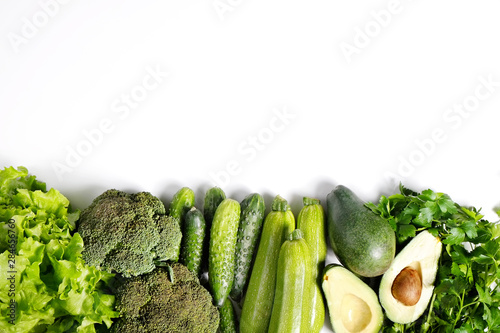 Bunch of greens and herbs laid on white countertop. Halved avocado  lettuce salad leaves  raw broccoli and other vegetables in row. Vegan diet concept. Close up  copy space  background  top view.