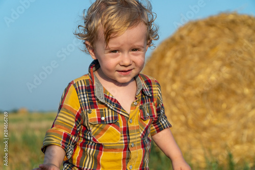 Little fair-haired boy playing on a wheat field with bales