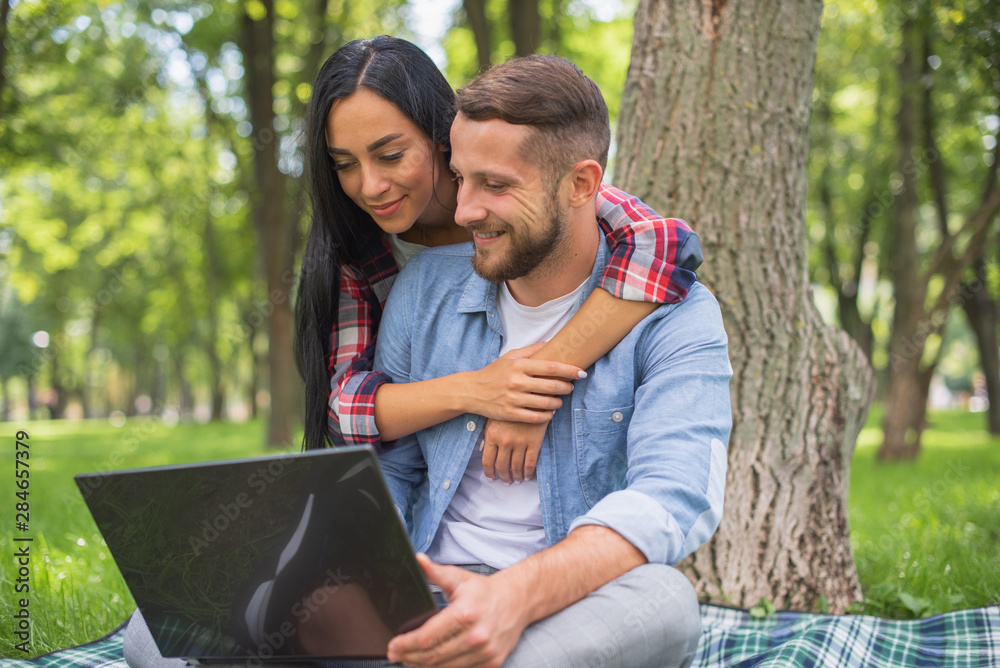 loving couple in the park are using a laptop, cuddling loving couple in the park are using a laptop, cuddling